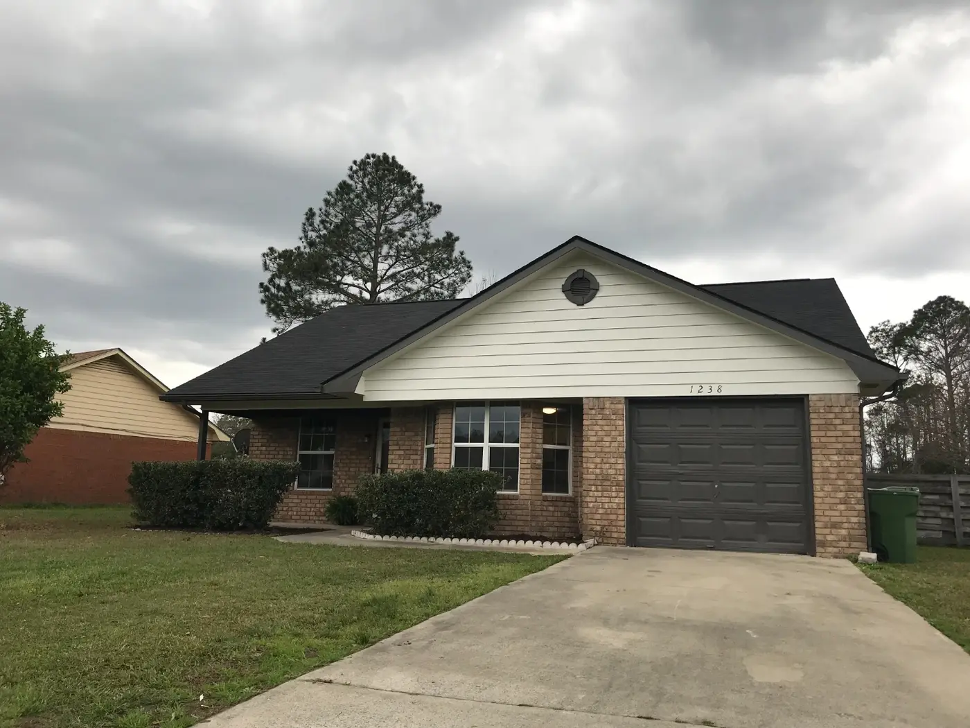 After: the same house with fresh white siding, a dark garage door, and a tidy front yard