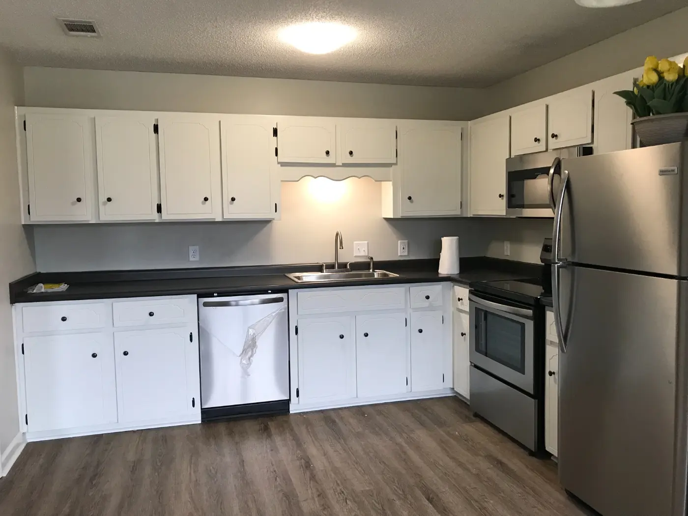 After: a renovated kitchen with white cabinets, dark countertops, and stainless steel appliances