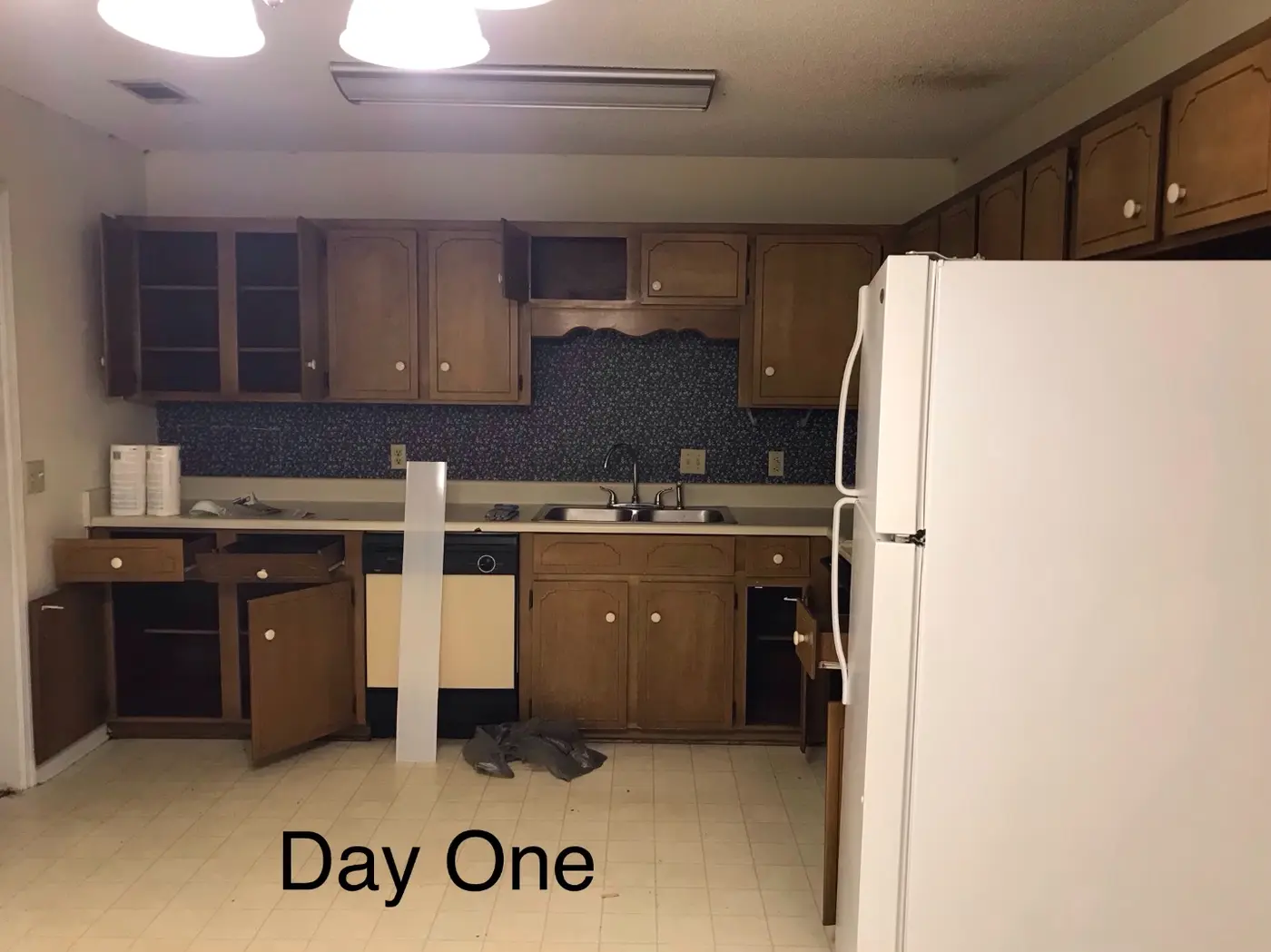 Before: a dated kitchen with brown cabinets, a navy floral backsplash, and tile flooring