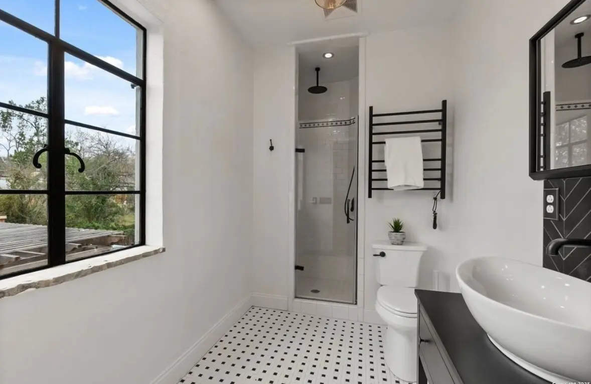 After: the finished bathroom with black fixtures, herringbone black tile accent, a black-framed window, and a radiator towel warmer