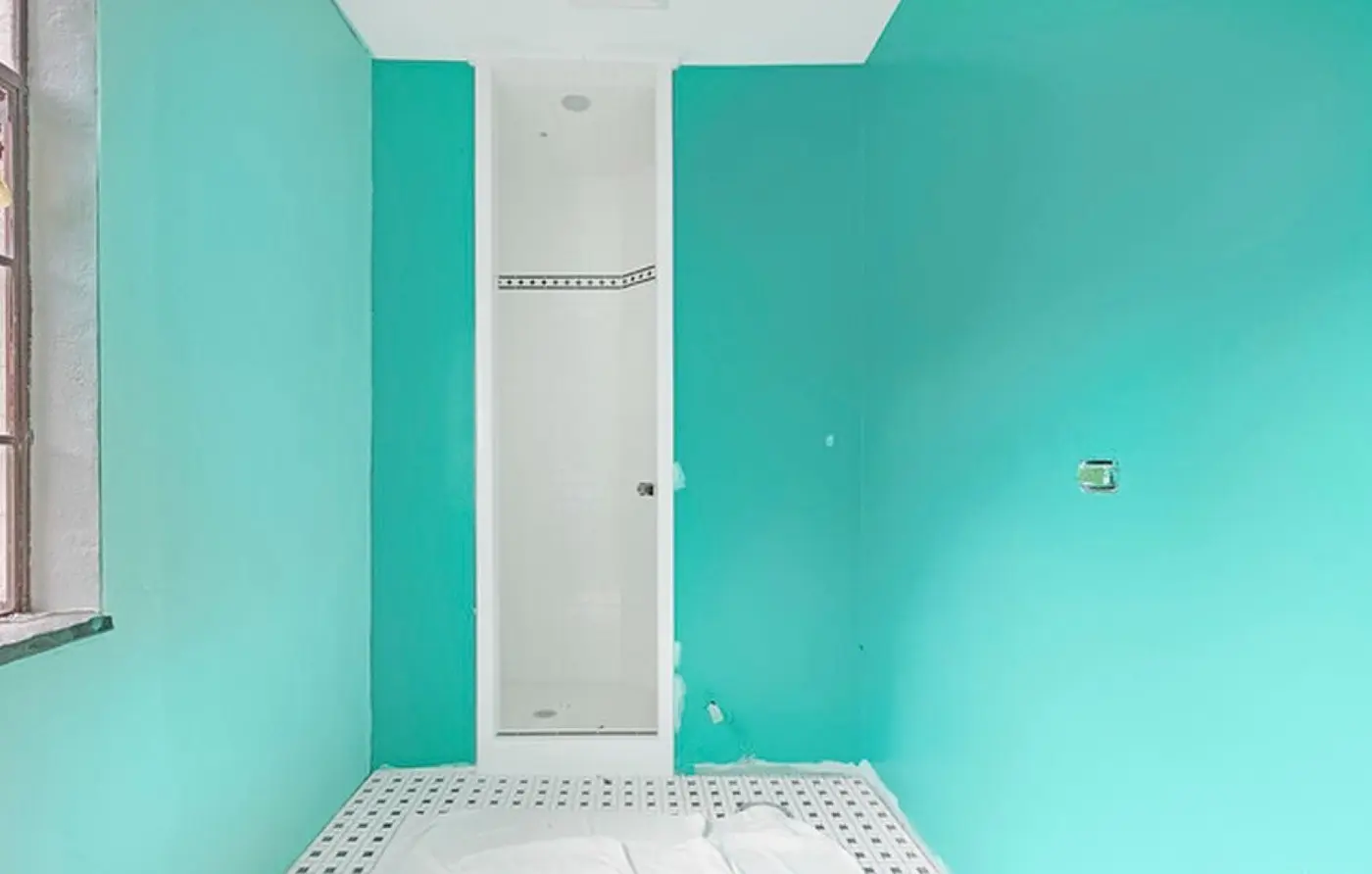 Before: a bathroom with bright teal walls, an unfinished shower stall, and an exposed outlet