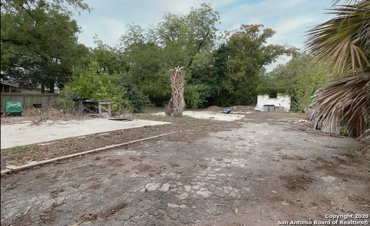 Before: bare dirt and a cracked concrete slab with a dilapidated white shed and a dead palm tree