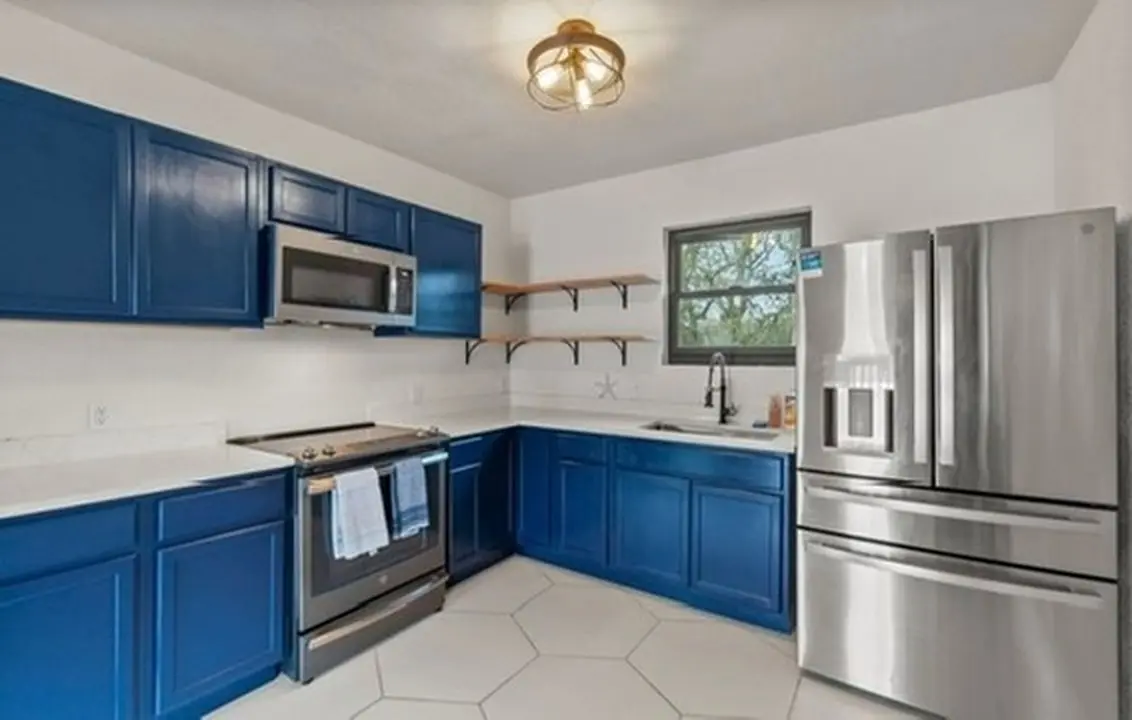 The finished guest kitchen with navy cabinets, quartz counters, stainless appliances, and a hexagon tile floor