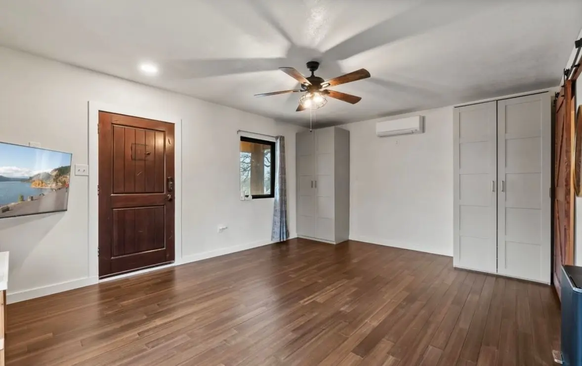 The finished guest living room with wood floors, a TV, a wardrobe, a mini-split unit, and a barn door