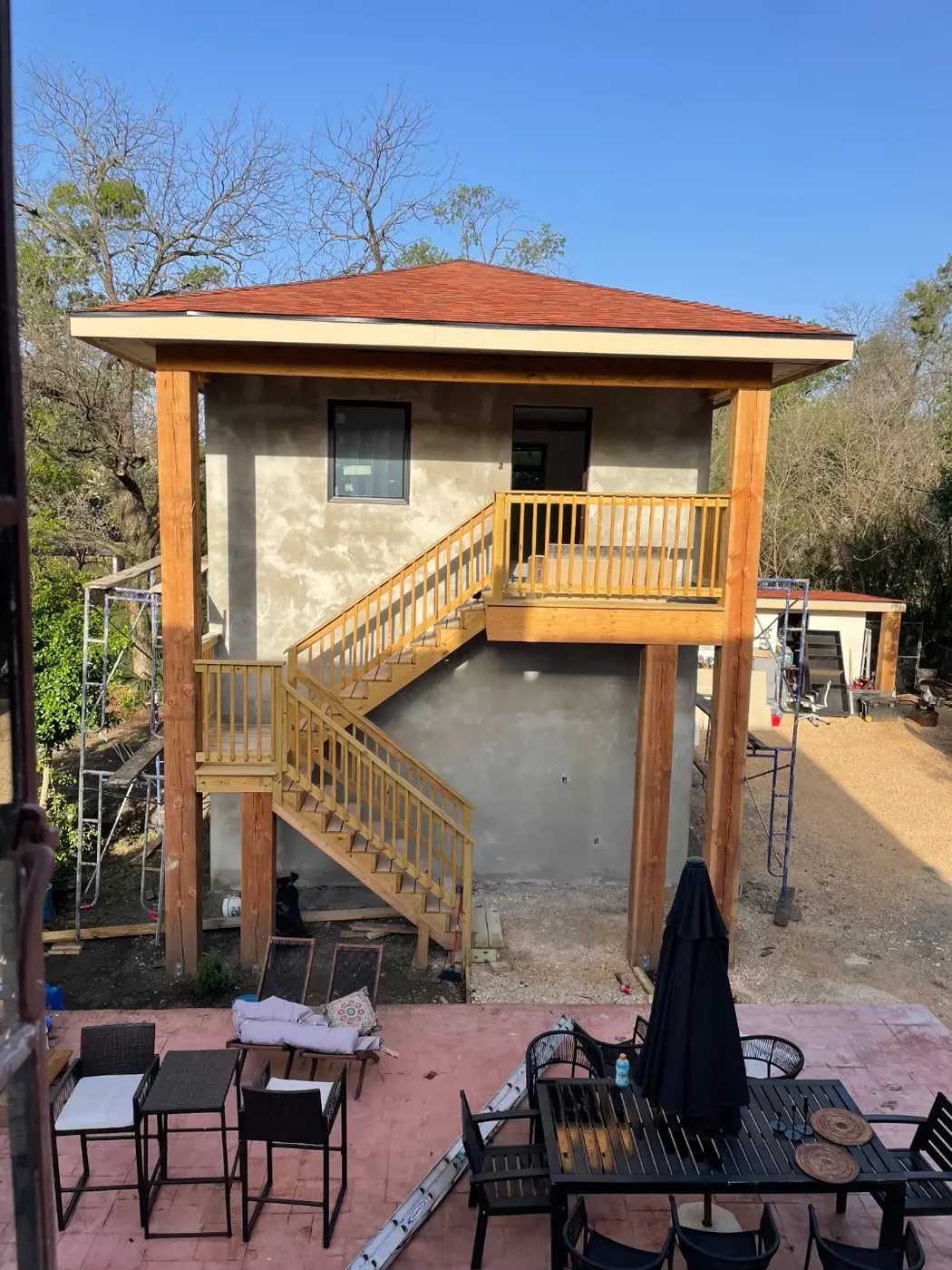 The two-story structure with roof on, gray plaster walls, and the wood exterior staircase built, seen from the backyard patio