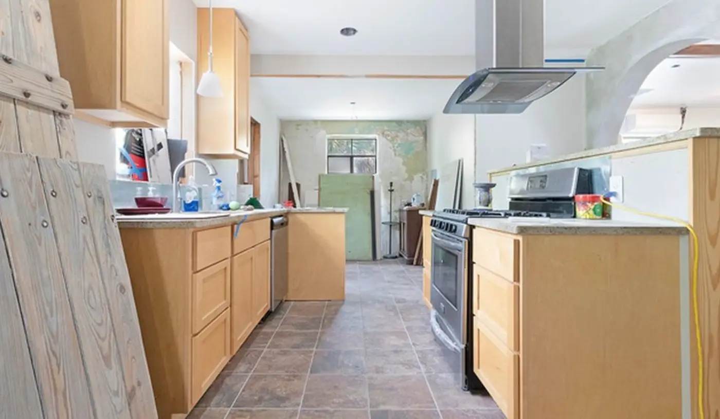 Before: an aged mint-green plaster wall exposed in a cluttered galley kitchen