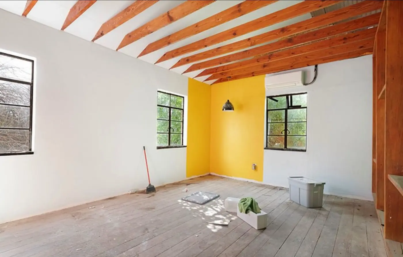 Before: an unfinished loft space with a bright yellow accent-wall paint test, exposed rafters, and bare wood subfloor