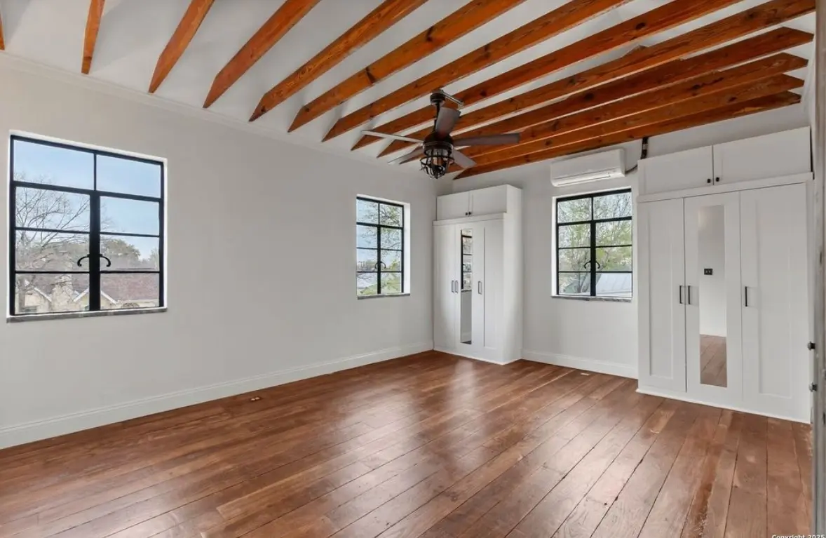 After: the finished secondary bedroom with a wood beam ceiling, white wardrobes, refinished dark hardwood floors, and a mini-split unit