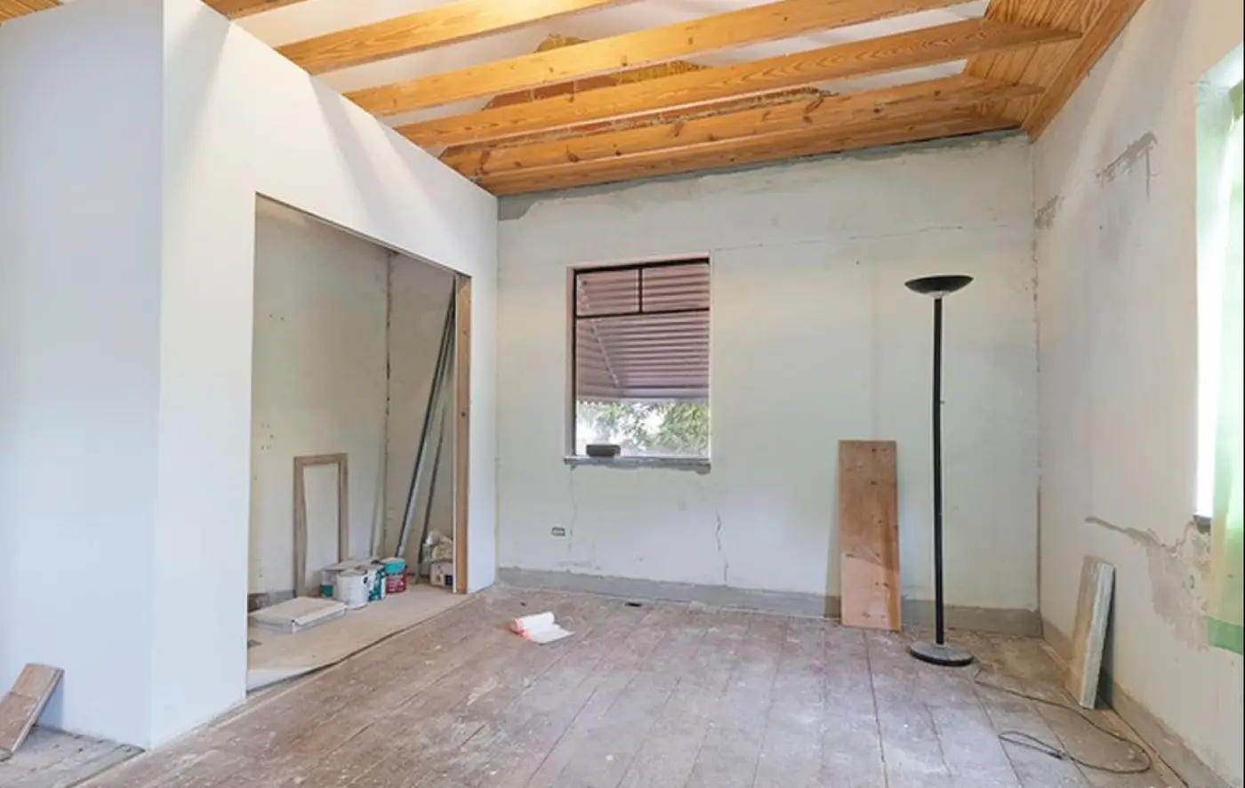 Before: the same secondary bedroom space, unfinished with exposed beams, bare concrete walls, and a plywood subfloor