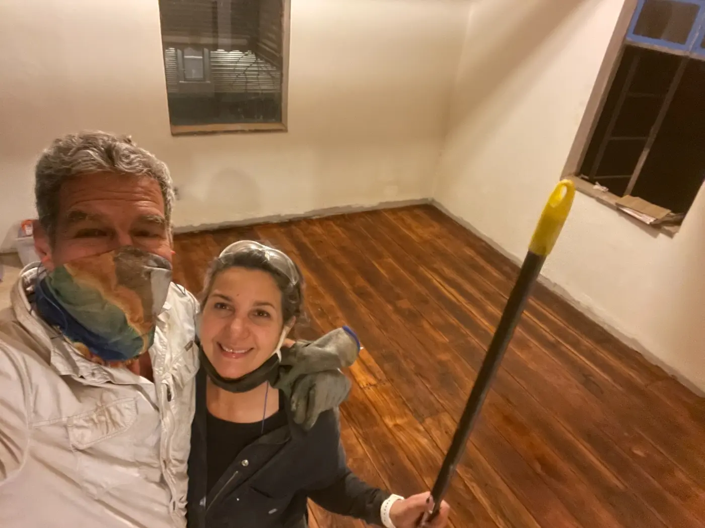 The two of us in masks, smiling, standing on the freshly stained wood floor
