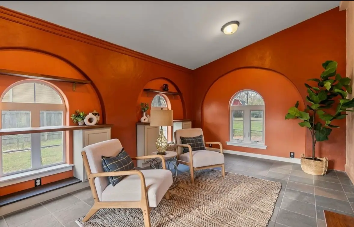 After: a sunroom painted a vivid burnt orange, with arched niches, built-in shelves, mid-century chairs, a jute rug, and a fiddle-leaf plant