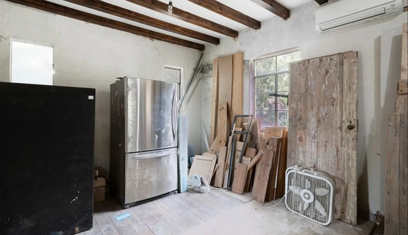 Before: the original dining room used as storage for building materials, with an exposed refrigerator and lumber stacked against the wall