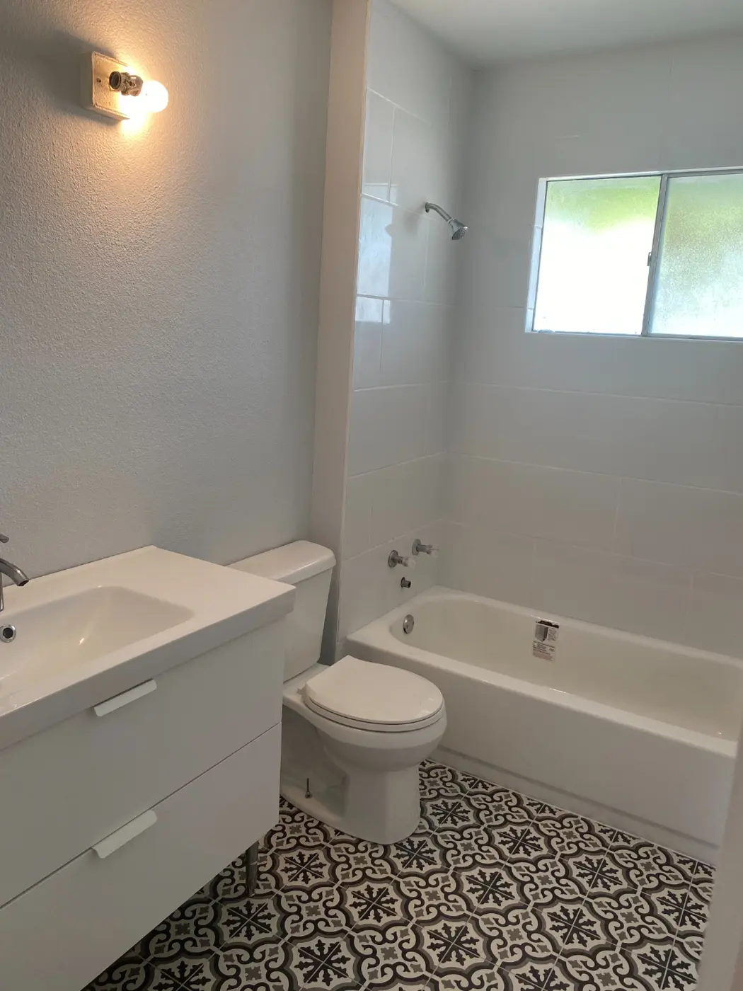 The finished bathroom with a white tile tub surround, patterned floor tile, a floating white vanity, and a new toilet