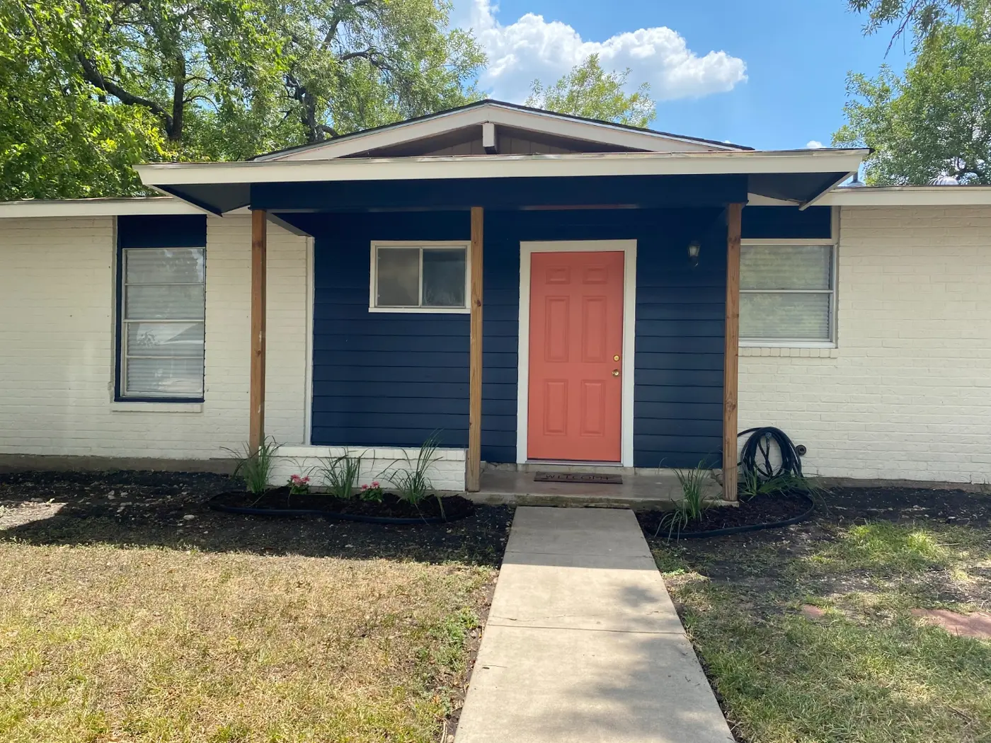 After: the same house with navy siding, a coral front door, whitewashed brick, and fresh landscaping