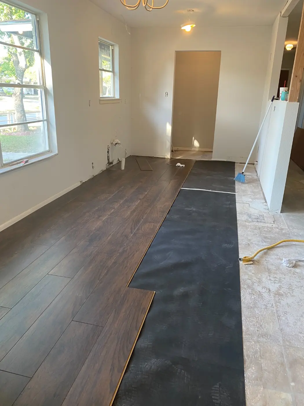 Dark brown vinyl plank flooring being installed over underlayment in a dining room