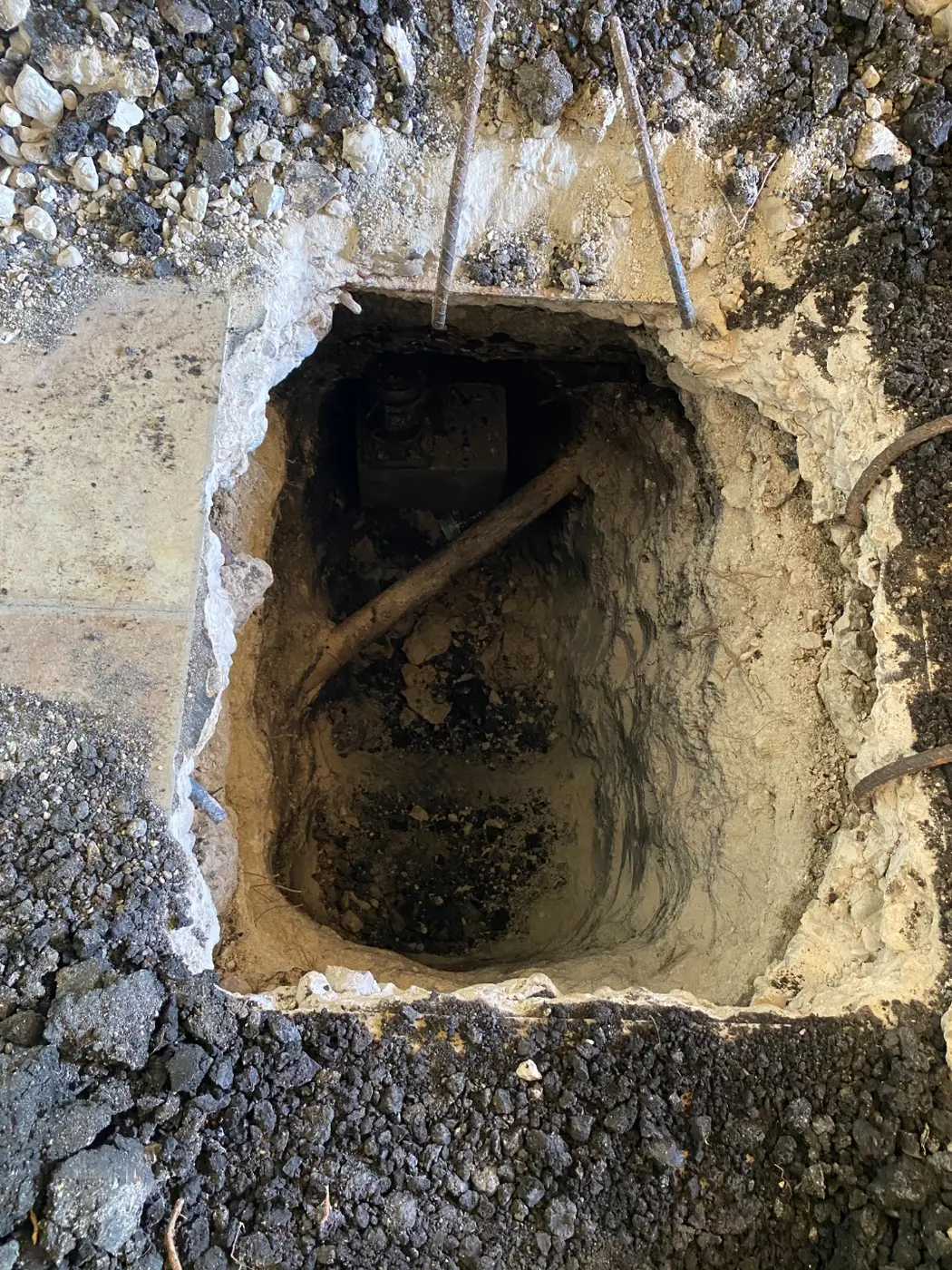 A deep excavation pit dug to access the foundation and plumbing beneath the house