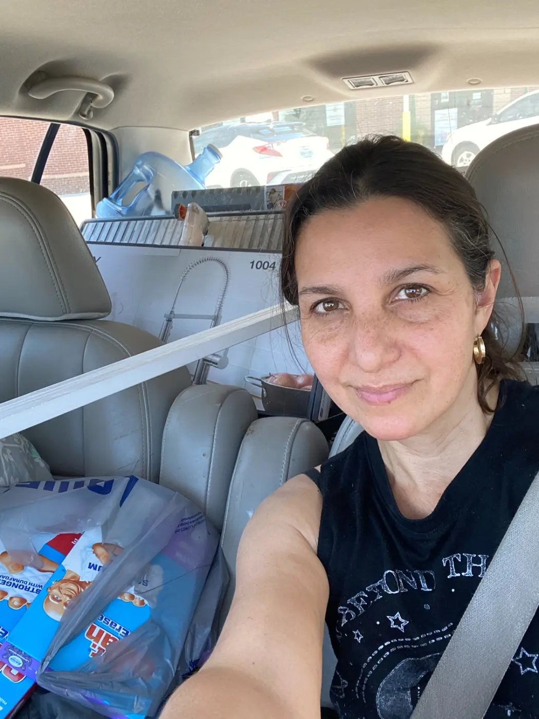 Selfie in the car packed with renovation supplies, including a faucet and lengths of pipe across the back seats