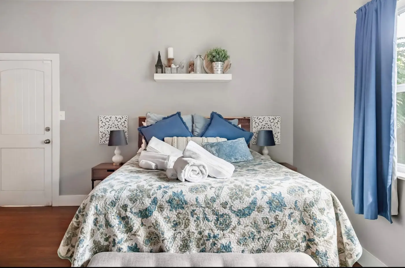 After: a bright bedroom with a floral quilt, blue accent pillows, and rolled white towels