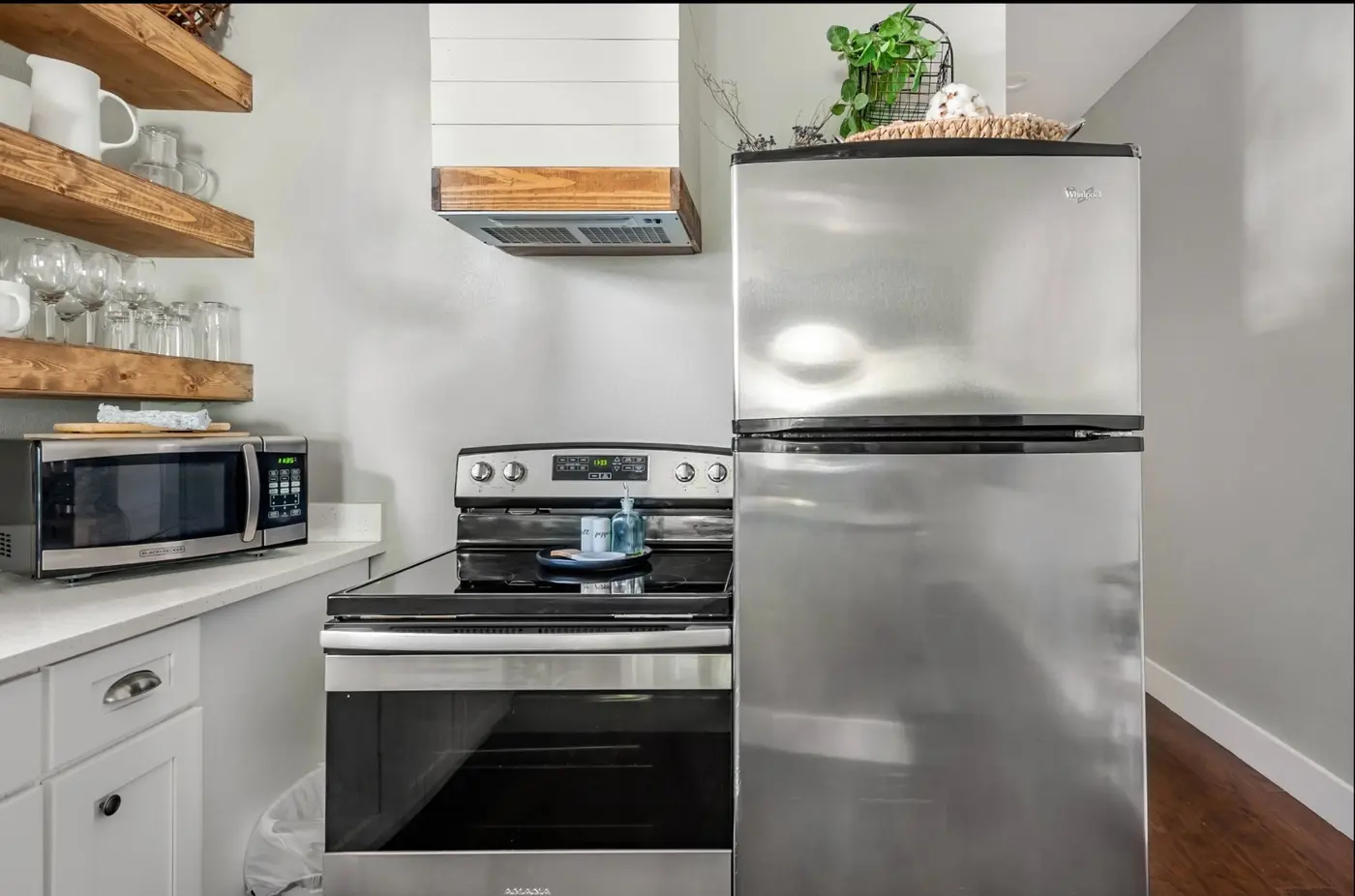 After: a bright kitchen with a stainless fridge, range, and open wood shelving with glassware