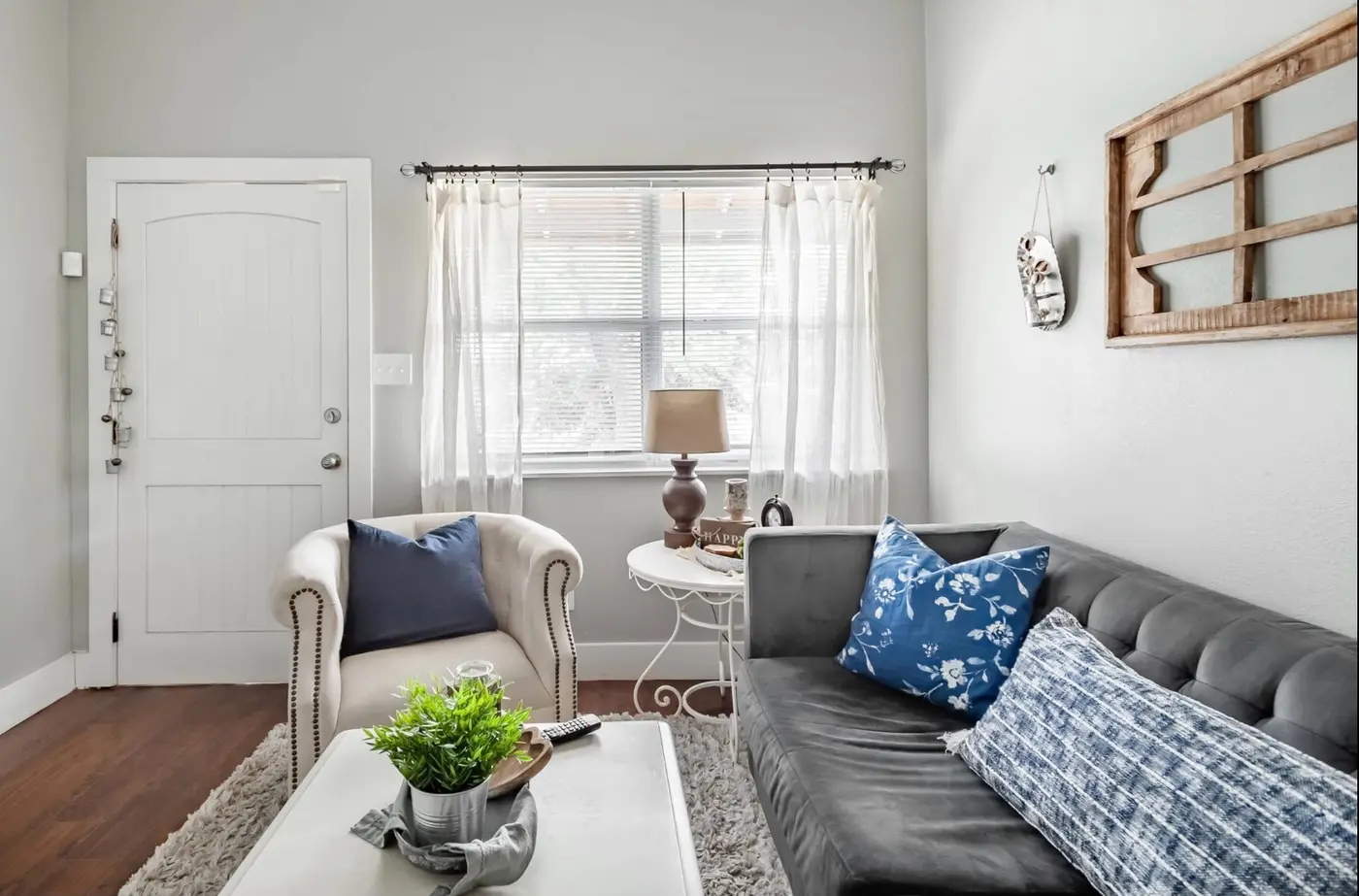 After: a sunlit living room with a tufted gray sofa, blue floral pillows, and a cream armchair