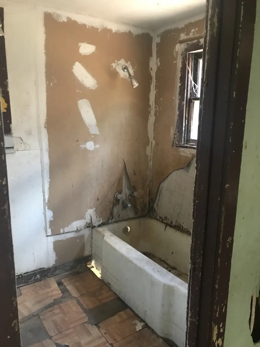 Before: a stripped bathroom with an old tub and exposed shower valve