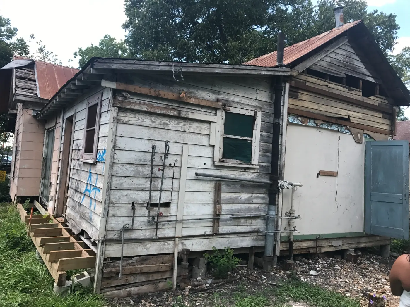Before: severely worn exterior siding with graffiti, a blue door, and makeshift wood stairs