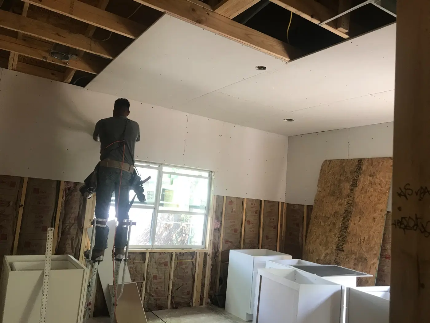 During: drywall going up over fresh insulation, with kitchen cabinets waiting nearby