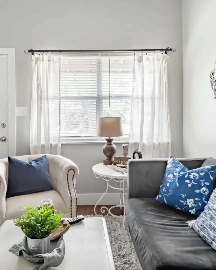 After: a furnished living room with a velvet sofa, cream armchair, and sheer curtains