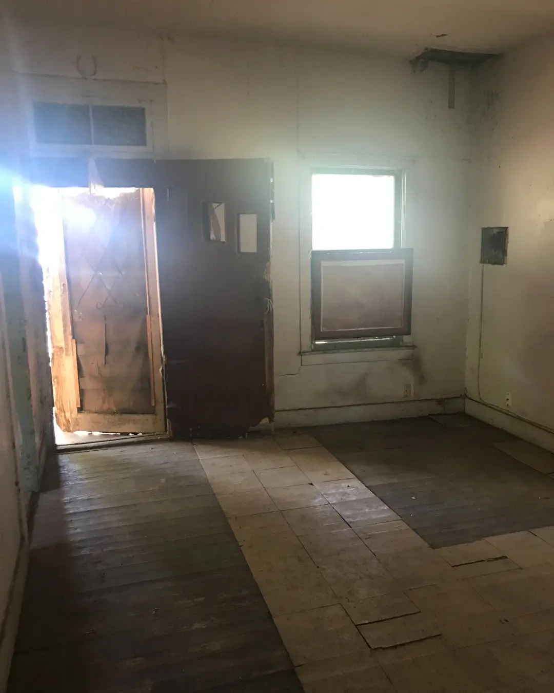 Before: a gutted room with worn hardwood floors and a heavy antique door