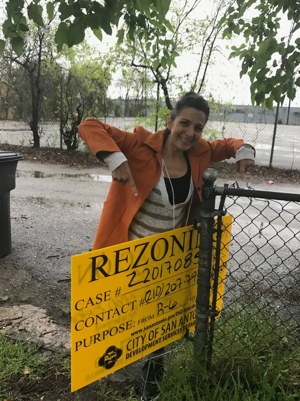 Anna smiling and pointing at the city rezoning sign on the property fence