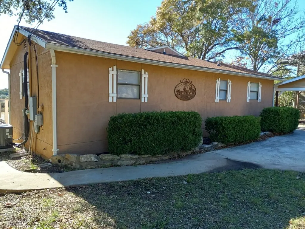 Before: side exterior view of the tan stucco house with a Texas star medallion on the shed
