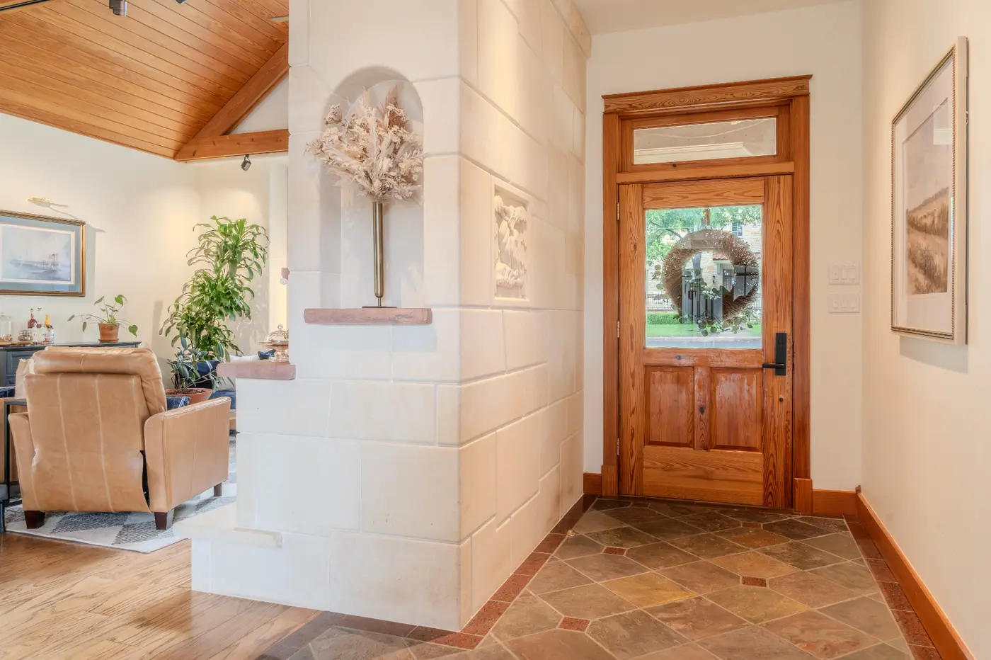 After: the same entryway warmed up with a leather chair, plants, framed art, and the same wood front door with its glass transom