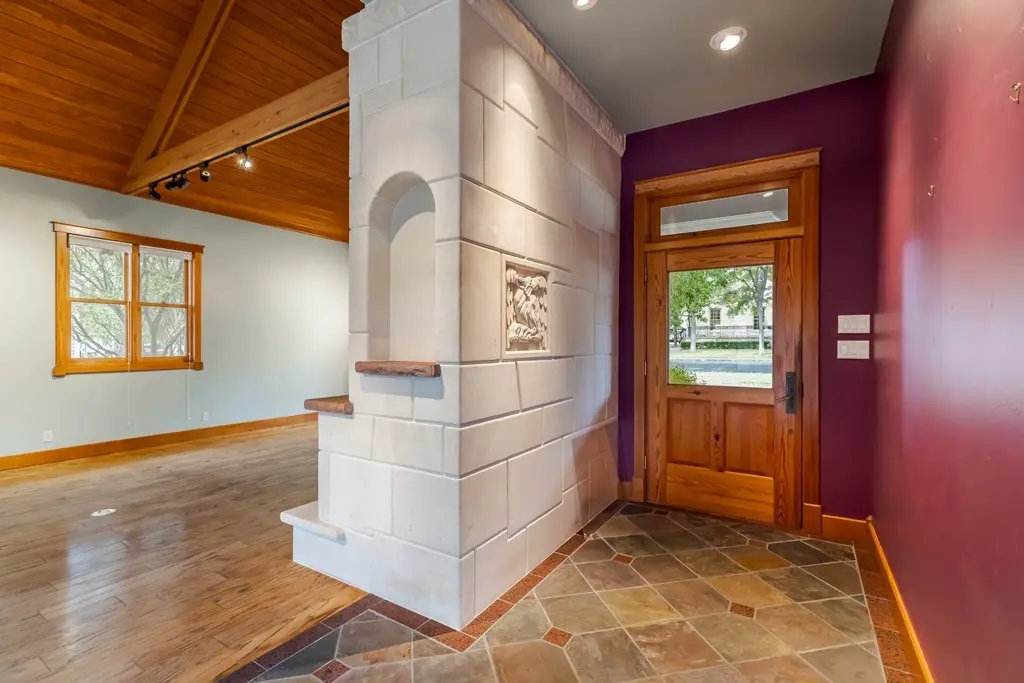 Before: an empty entryway with a tall stacked-stone chimney corner, purple and maroon walls, and a wood front door with a glass transom