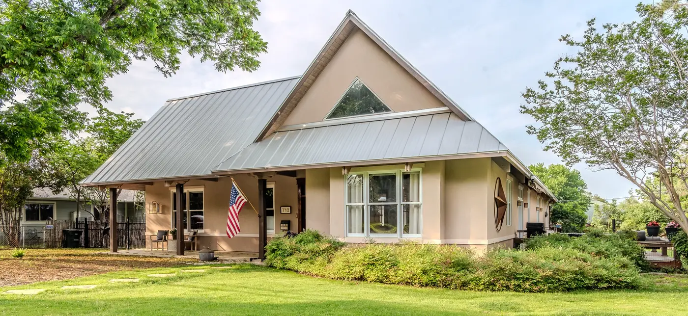 After: the same house with a lush full lawn, mature landscaping, and an American flag on the front porch
