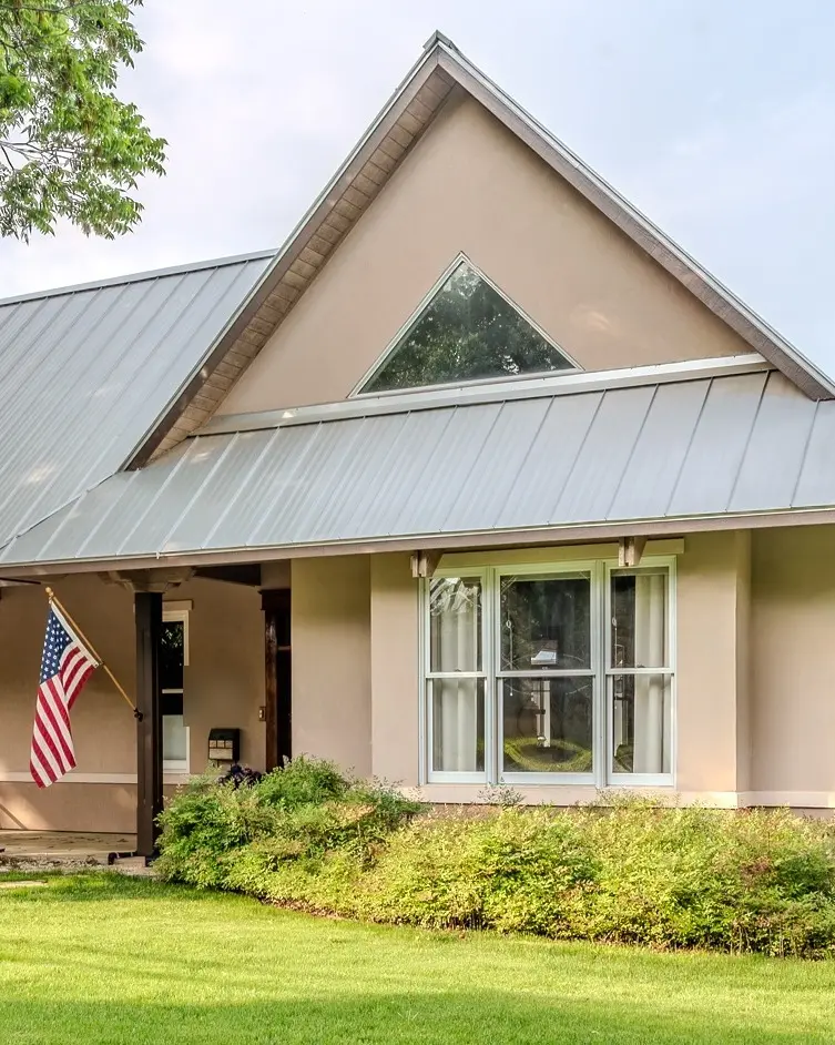 The finished exterior of the Travis, Fredericksburg house, with a metal roof, front porch, and American flag