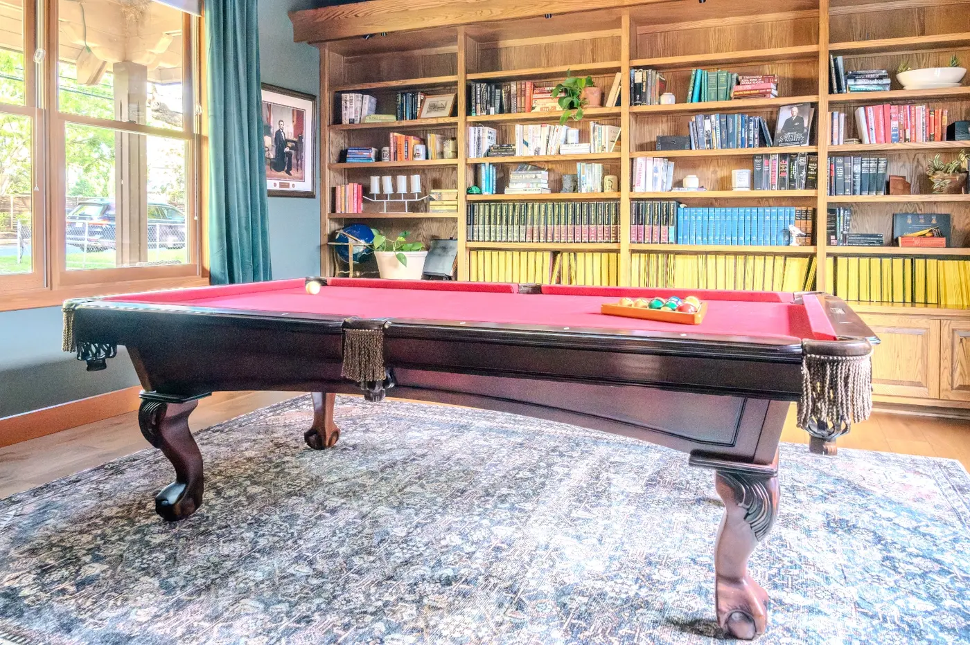 After: the same room turned into a library and game room, with filled bookshelves and a pool table, under the same vaulted wood beams