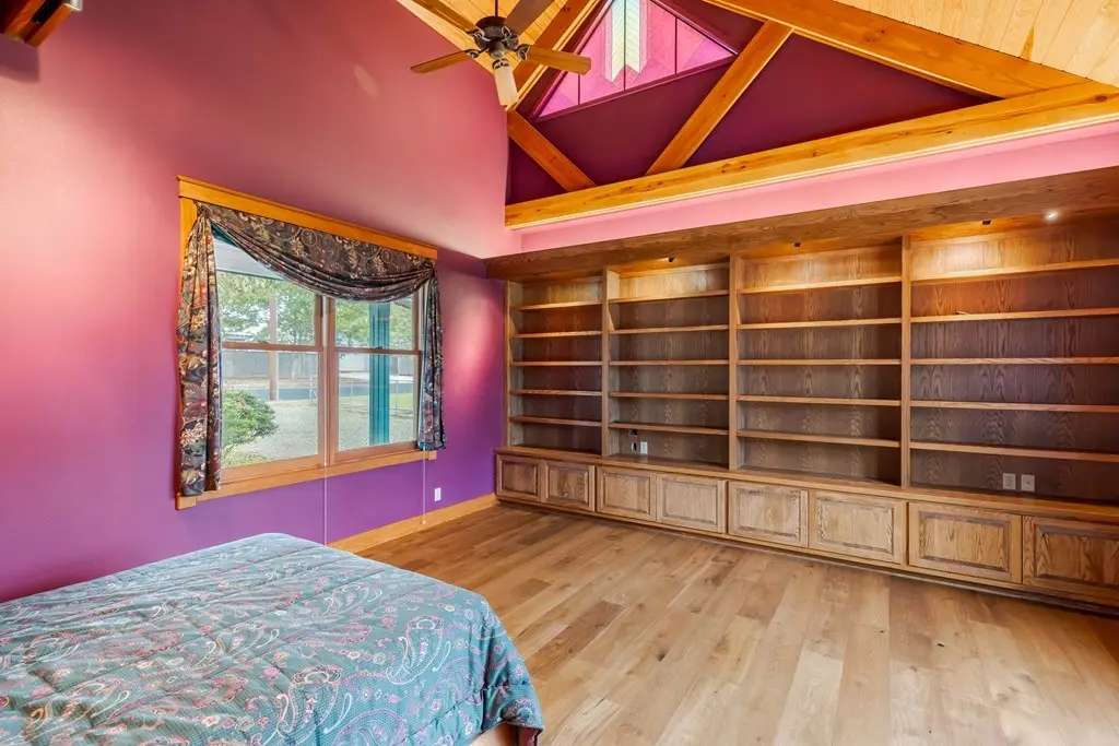 Before: an empty room with deep purple walls, a bare window, and unfinished built-in wood shelving under vaulted wood beams