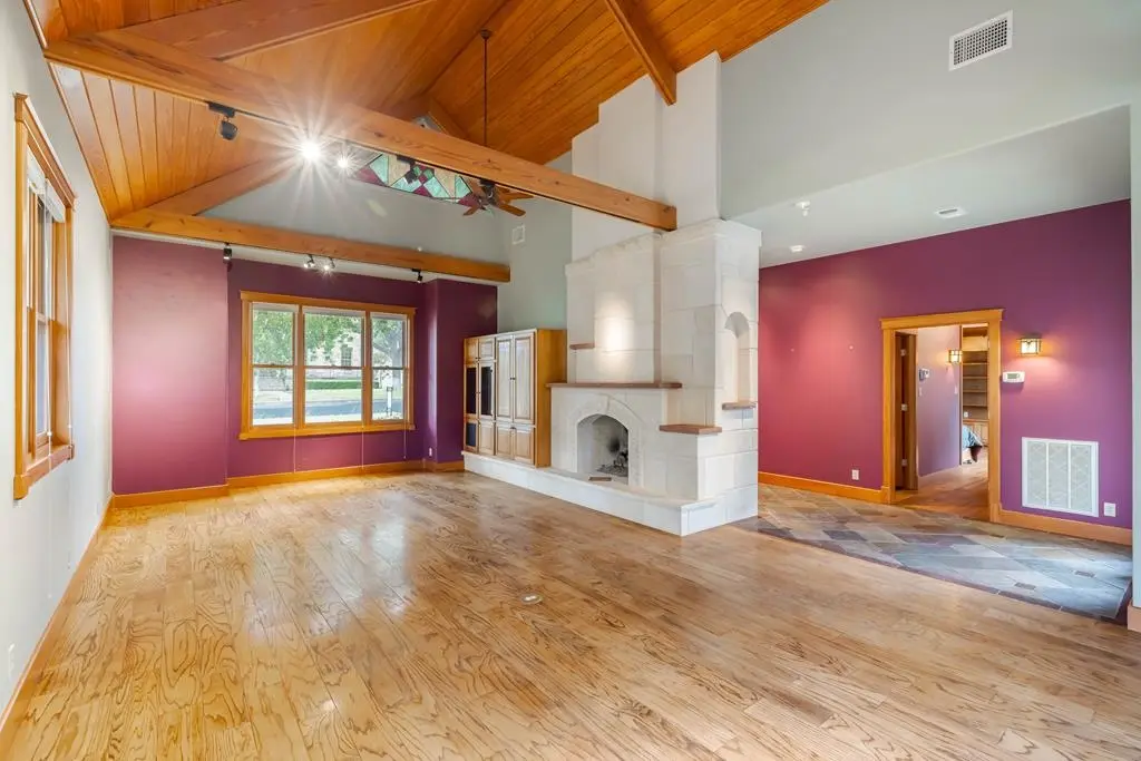 Before: an empty living room with a dramatic carved stone fireplace, maroon walls, and a wood beam ceiling